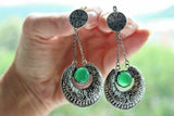 These are not your everyday earrings; they're a statement. Long and flowing in a captivating gypsy style, these earrings immediately draw the eye. Each features a verdant green jadeite, a natural and genuine gemstone revered for its rich color and captivating energy. The jadeite, a stone associated with harmony and balance, is showcased beautifully within a meticulously designed setting.