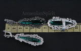 A pair of long silver earrings featuring marcasite and emerald green topaz, set against a dark background.