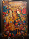A colorful religious icon painting of the Virgin Mary holding the infant Jesus, displayed upright on a clear stand against a dark background. Detailed religious artwork of the Blessed Virgin Mary wearing a crown next to Baby Jesus, decorated with rich floral patterns and heavenly angels.