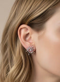 Close-up of an ear wearing a sun-shaped earring with a pearl center.