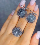 Silver mandala-style Armenian ethnic earrings on a hand with light pink nail polish against a neutral background