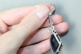 Silver earring with a black gemstone held in a hand against a neutral background