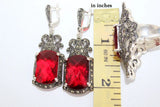Red gemstone and marcasite earrings with silver accents next to a ruler showing their size.