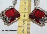 Red gemstone earrings with marcasite floral accents on a measuring tape