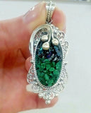 Silver filigree pendant with drusy green malachite gemstone held in a hand against a white background