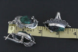 Silver jewelry with green malachite gemstones on a black background with a ruler for scale.