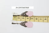 Pair of earrings with pink stones and marcasite elements on a ruler for scale, with 'IN CENTIMETRES' text above.