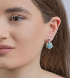 Close-up of a woman wearing a gold plated Armenian handmade earring with a sky blue larimar  gemstone.