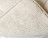 Close-up of a soft cream fleece or sheep skin blanket with a folded corner revealing a white layer underneath. 