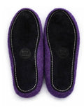 A pair of purple wool felt slippers shown from the bottom, featuring a black suede-like footbed with white contrast stitching and a circular brand logo. 