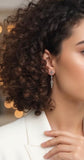 Close-up of Armenian woman with styled hair and long Armenian small cross earrings against a blurred background