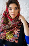 An elegant woman wrapped in a traditional, opaque merino wool scarf featuring detailed Slavic patterns and a rich red color palette.