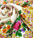 Close-up detail of a premium ivory merino wool scarf, showcasing its soft, textured weave. The shawl is decorated with a vibrant, multicolored floral print including orange, pink, and yellow flowers, providing a cozy and traditional winter fashion look.