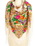 A traditional Slavic-style merino wool shawl in ivory, wrapped like a warm blanket. The oversized garment features a striking contrast between the neutral ivory background and the bright, detailed patterns of yellow, orange, and pink flowers, complete with intricate fringe detailing. 