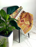 Decorative carpet with geometric pattern Armenian draped over a green chair next to a plant on a white floor.