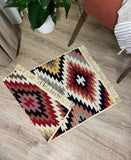 Two patterned traditional rugs on a wooden floor with a plant and chair in the background.