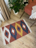 Decorative Armenian rug with geometric red and yellow pattern on a wooden floor, next to a plant and chair.