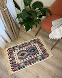 Decorative Armenian carpet kilim with geometric pattern on a wooden floor, chair, and plant in the background.