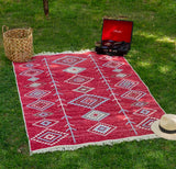 Red patterned Armenian rug on grass with a vinyl record player and hat. Buy Armenian cafe decor for covering the floor or sofas.