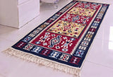 Traditional Armenian caret with fringes and ethnic taraz diamond ornaments in red, blue and beige on a white floor.