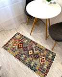 A rectangular area rug with a colorful geometric tribal pattern in red, green, yellow, and beige, styled on a light wood floor in a dining room setting next to a white table and chairs.