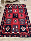 A rectangular machine-woven kilim rug with a geometric Armenian pattern, featuring red, navy blue, beige, and white blocks with tribal symbols, shown on a light wood floor.