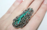 Decorative large full finger ring with emerald long stone green gemstone on a hand against a white background