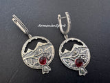 Silver earrings with circular designs and red stones on a dark background