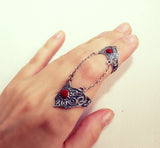 A double ring with connected chains and burgundy red enamel dots on a sterling silver 9251 ring, displayed on a person's hand.