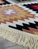 Close-up of a red patterned rug with fringes on a wooden floor