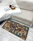 A rectangular area rug with a multicolor geometric tribal pattern lies on a light gray wood floor in front of a cream-colored sofa with a white throw blanket.