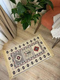 Decorative Armenian rug with geometric pattern on a wooden floor, next to a plant and chair.
