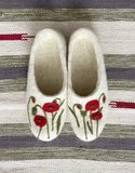 Pair of white woolen slippers with red floral design on a striped fabric background