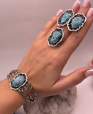 Hand wearing a bracelet , a ring and earrings with blue natural turquoise stone accents on a neutral background