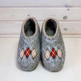 Woolen slip on slippers like indoor shoes for men in large size with rhombus design in red and beige on a wooden floor.