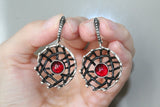 A set of sterling silver jewelry including oxidized black net design earrings and a matching ring, each adorned with a red garnet stone.