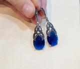 A pair of royal blue topaz earrings with marcasite accents, crafted in sterling silver 925, held in a person's hand.
