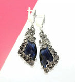 Pair of earrings with blue gemstones and silver detailing on a white and pink background