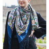 Person wearing a colorful patterned oversized blue scarf with along silky fringe.
