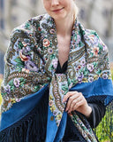Woman wearing a colorful floral  patterned blue merino wool shawl with long fringe.
