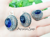 A pair of silver dome earrings with blue stones, held in a hand against a white background.