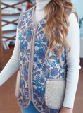 A woman wearing a sleeveless blue and white floral-patterned merino wool vest over a white long-sleeve top.