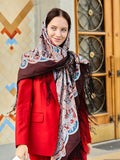 A woman wearing this merino wool shawl enjoys its generous size and natural warmth. The brown base with light blue and red Slavic patterns and silky fringe create a balanced, traditional look.