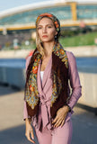 An extra-large natural merino scarf styled on a woman, featuring an intricate herbal pattern in warm green and brown hues. The retro-inspired design and flowing silky fringe create a refined yet organic look.