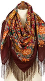 Colorful orange floral-patterned merino wool brown scarf with fringes on a mannequin against a white background. The scarf features a clean brown base adorned with heavy patterns of vibrant orange flowers, golden-yellow scrolls, small green leaves, and detailed silky fringes.