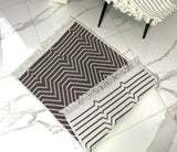 Black and white geometric patterned rug with tassels on a marble floor.