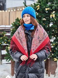 Person wearing a blue knit hat and red patterned woolen scarf in front of Christmas trees.
