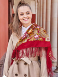 This 100% merino wool Slavic shawl is crafted from natural sheep wool. A woman wears the red fringed shawl adorned with peonies in yellow and pink.