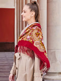 A woman wearing a beautiful Slavic-style shawl woven from 100% merino wool. The natural sheep wool features fringe details and peony flowers in soft yellow and pink on a red base.