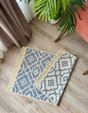 Two patterned rugs on a wooden floor with a plant in the background.